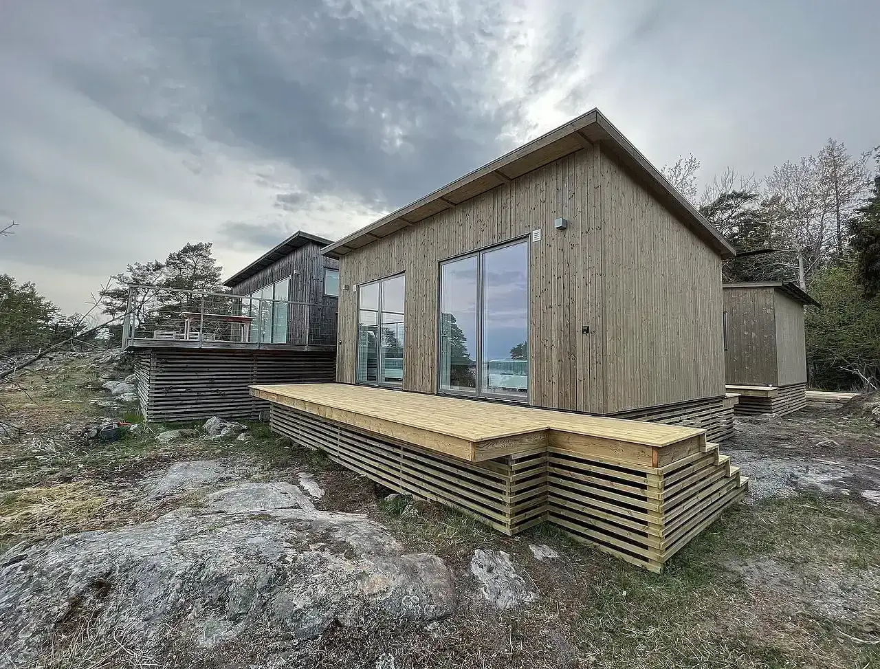 Modern träfasad med stora fönster och uteplats vid klippstrand.