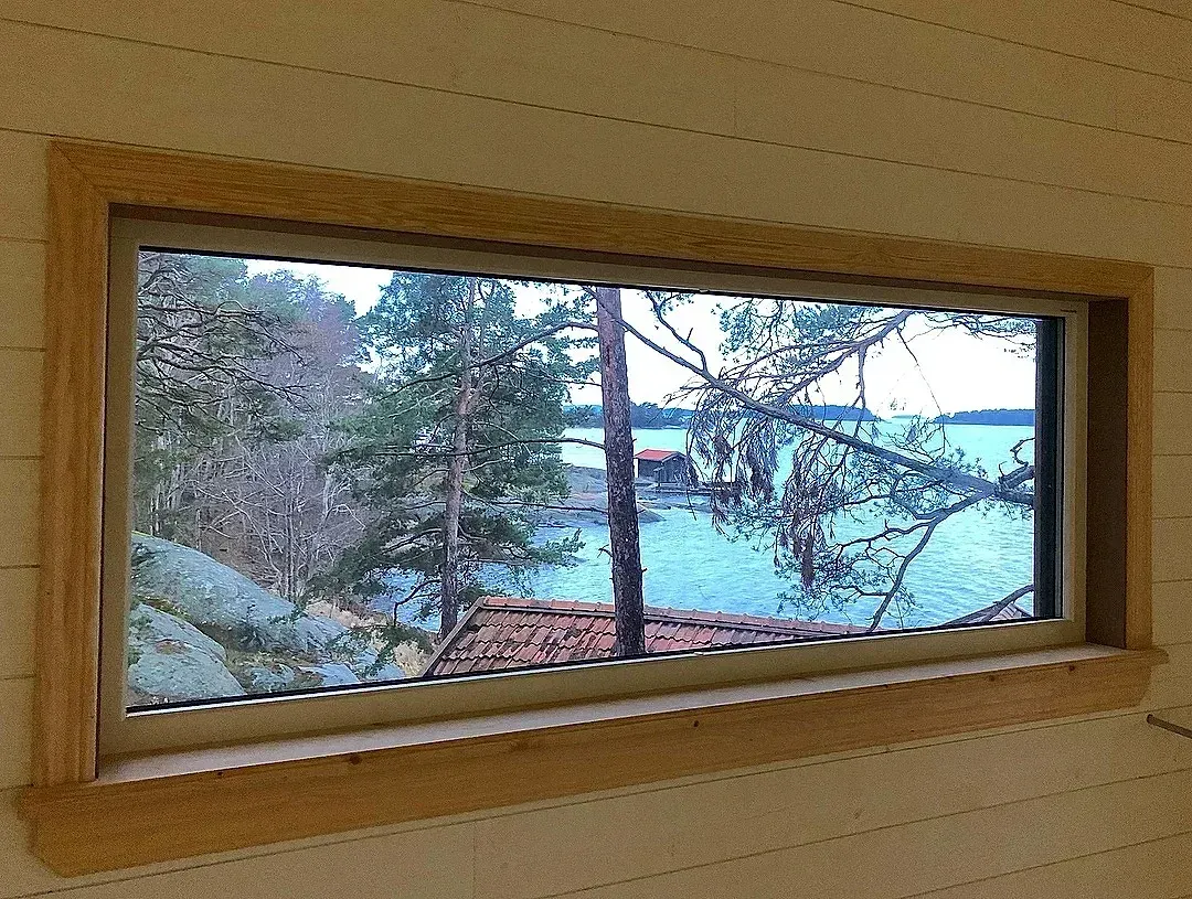 Panoramafönster med utsikt över skärgårdslandskap med träd och vatten.