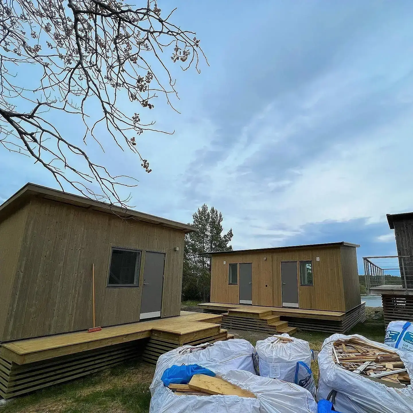 Trä modulhus under konstruktion med byggmaterial i förgrunden under molnig himmel.