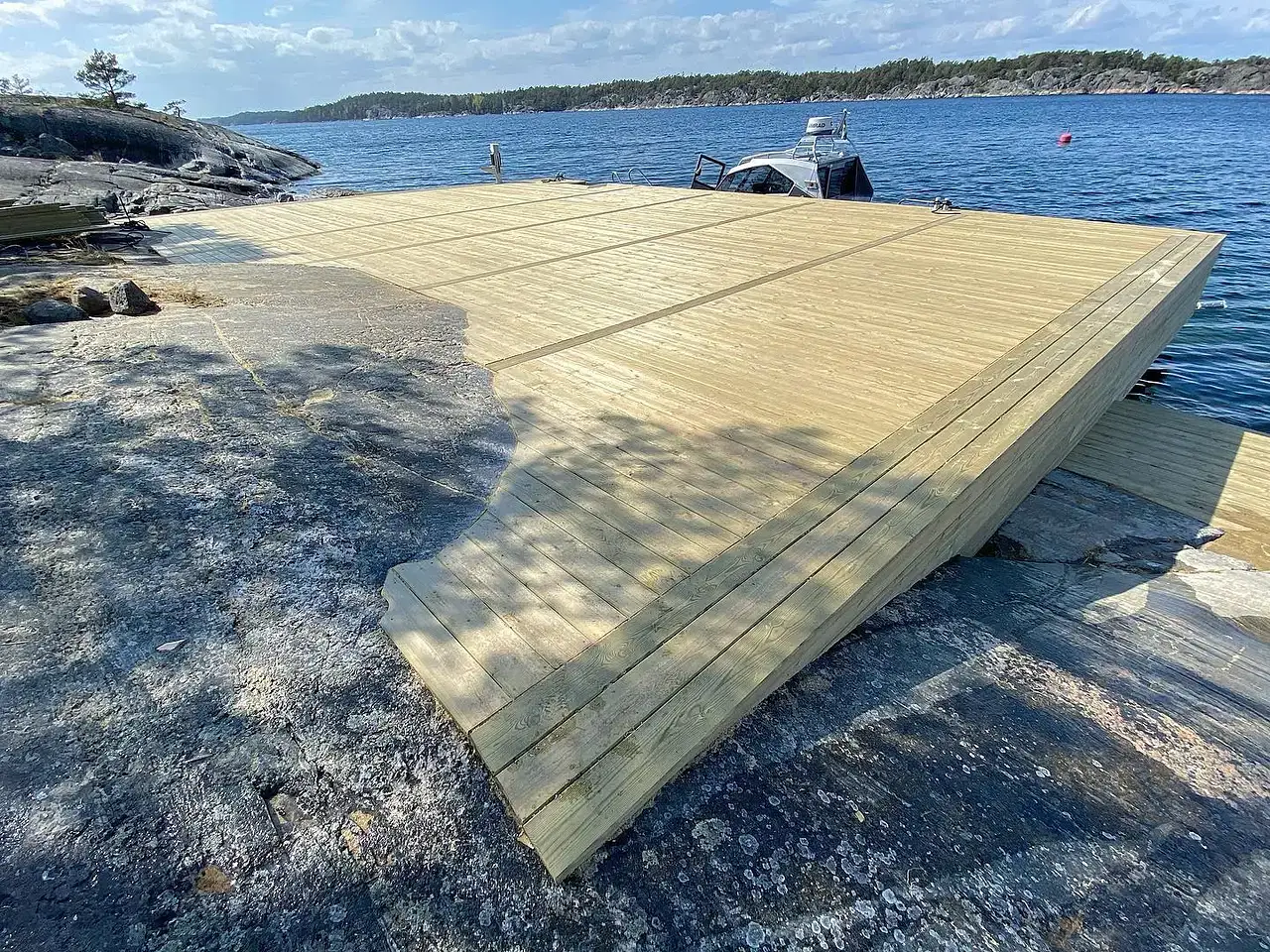 Ny träbrygga på klippstrand med båt förtöjd vid vattnet.